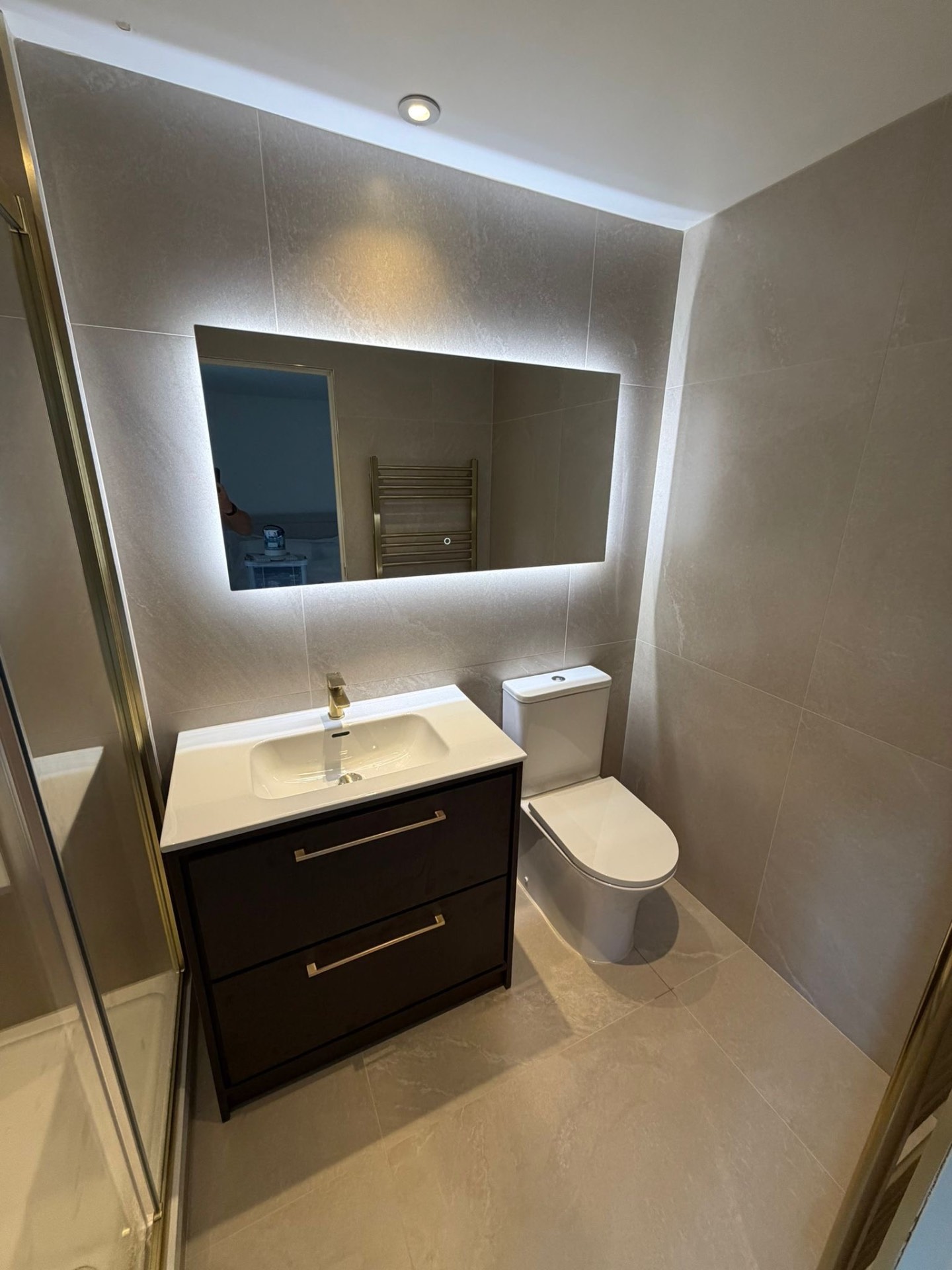 Modern ensuite with illuminated mirror, dark vanity and neutral stone tiling in Reading